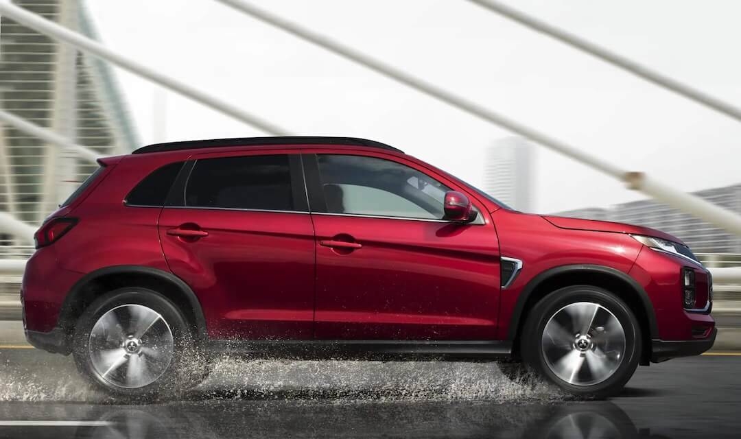 Vue latérale du Mitsubishi RVR 2026 rouge roulant sous la pluie.